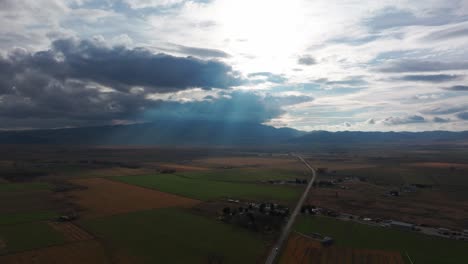 Drohnenaufnahme-Von-Sonnenlicht,-Das-Durch-Wolken-Kommt,-Mit-Bergen-In-Der-Ferne