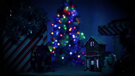 Camera-slowing-pushes-towards-a-little,-cute-Christmas-village-covered-in-snow-as-a-large,-well-lit,-beautiful-Christmas-tree-sits-in-the-background,-out-of-focus