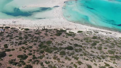 Drone-view-in-Greece-flying-over-balos-beach-with-clear-blue-sea-water-on-the-sides-and-white-sand-surrounded-by-brown-landscape-on-a-sunny-day-in-Crete