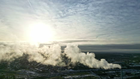Industrial-smog-from-a-chimney-with-cityscape-background,-sunny-day---Aerial-view
