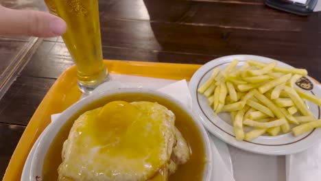 Francesinha-with-egg-and-typical-Portuguese-sauce,-accompanied-by-french-fries-and-a-cold-draft-beer