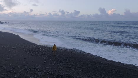 Aerial-panning-with-drone-on-young-man-walking-on-the-beach-at-sunrise,-Azores