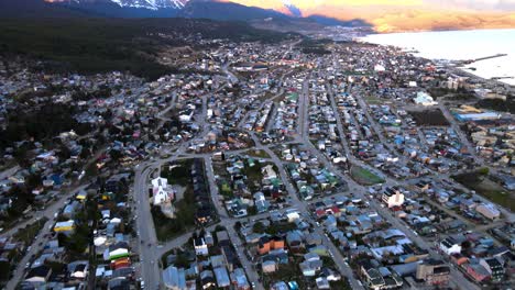 Drone-shot-flying-over-Ushuaia,-Argentina-while-panning-up-to-reveal-the-Andes-mountains-lit-by-the-sunset