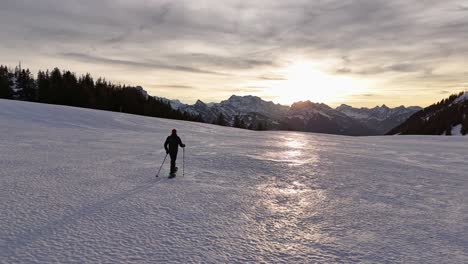 Aerial-tracking-shot-of-mountaineer-walking-on-snowy-slope-during-sunrise-in-the-morning---Swiss-Alps,-Amden