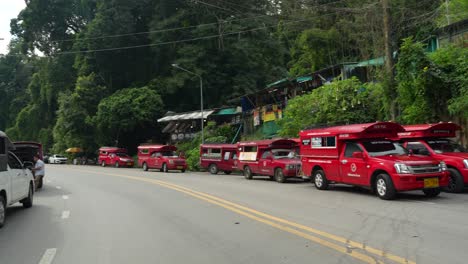 Larga-Fila-De-Camiones-De-Transporte-Songthaew-Rojos-Estacionados-A-Lo-Largo-De-Una-Carretera-Selvática