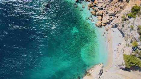 Drone-top-down-static-view-of-turquoise-water-and-rocky-coast-by-white-sandy-beach