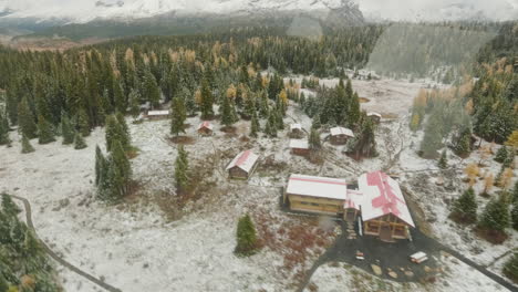 Aerial-view-filmed-from-a-flying-helicopter-showing-a-vibrant,-snowy-wilderness-backcountry,-cabins-and-surrounding-mountains-are-covered-in-snow