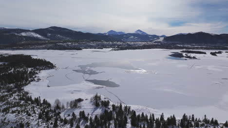 Downtown-Frisco-toward-Keystone-Colorado-aerial-cinematic-drone-Lake-Dillon-Marina-Summit-cove-cloudy-snowy-winter-morning-view-Silverthorne-Ten-Mile-Range-Breckenridge-calm-unfrozen-ice-circle-left