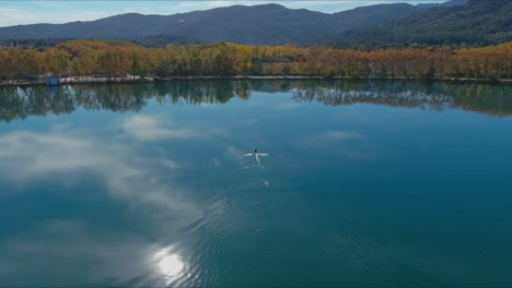 Lake-Banyoles-autumn-reflects-sky-and-sun-as-rowboat-moves-to-shore