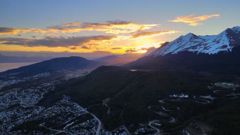 Drone-shot-flying-over-Ushuaia,-Argentina-towards-a-dramatic-sunset-in-the-Andes-mountains