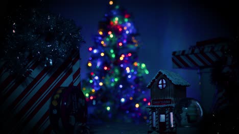 Camera-slowing-pulling-away-from-a-little,-cute-Christmas-village-covered-in-snow-as-a-large,-well-lit,-beautiful-Christmas-tree-sits-in-the-background,-out-of-focus