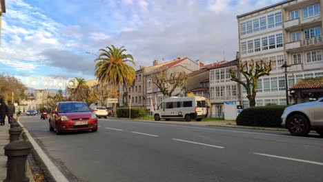 combustion-engine-vehicles-driving-down-city-avenue-with-palm-trees-on-a-cold-winter-day-with-clouds-in-the-sky,-shot-blocked,-Santiago-de-Compostela,-Galicia,-Spain