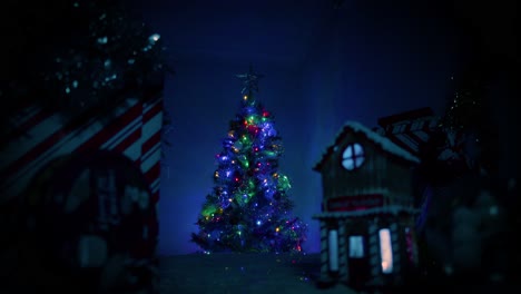 Camera-slowing-pushes-towards-a-beautiful,-well-lit-Christmas-tree-sitting-behind-a-small,-cute-Christmas-village-that-sits-out-of-focus-in-front-of-camera