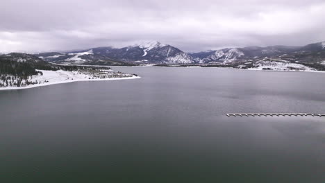 Lake-Dillon-Marina-Colorado-aerial-cinematic-drone-cloudy-snowy-winter-morning-view-Frisco-Breckenridge-Silverthorne-Ten-Mile-Range-peaceful-calm-reflective-frozen-ice-backward-motion
