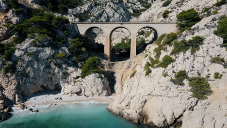 Aerial-orbit-around-tall-arched-bridge-crossing-white-rocks-off-coast-of-Calanque-de-l’Everine-France