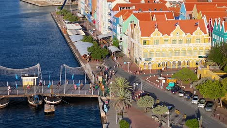 Luftaufnahme,-Die-Einen-Überblick-über-Touristen-Gibt,-Die-Entlang-Der-Königin-Emma-Brücke-Unter-Den-Lebhaften-Gebäuden-Des-UNESCO-Weltkulturerbes-In-Curaçao-Spazieren