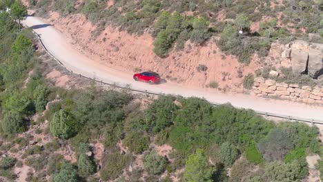 Aerial-view-of-red-car-driving-through-mountains-on-rural-road