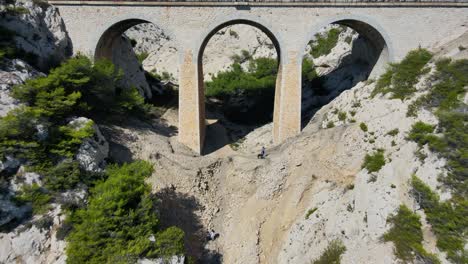Drone-pullback-from-historic-tall-arches-as-explorers-hike-on-coast-of-France