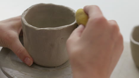 Masterfully-shaping-clay-into-a-cup-using-a-turning-wheel-and-sponge,-a-mesmerizing-display-of-skill