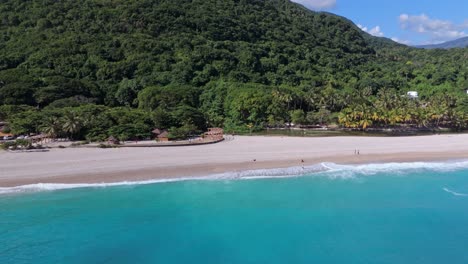 Panorama-drone-shot-of-tourist-relaxing-at-sand-beach-in-front-of-tropical-mountains-in-summer-season