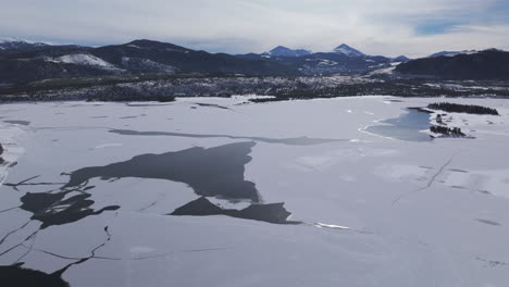 Downtown-Frisco-toward-Keystone-Colorado-aerial-cinematic-drone-Lake-Dillon-Marina-Summit-cove-cloudy-snowy-winter-morning-view-Silverthorne-Ten-Mile-Range-Breckenridge-calm-unfrozen-ice-backwards-up