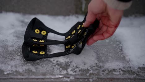 Person-places-pair-of-micro-spikes-for-shoes-on-icy-sidewalk