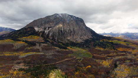 Dramatic-cloudy-autumn-Aspen-Tree-fall-colors-Kebler-Pass-trailhead-aerial-cinematic-drone-snow-on-peaks-landscape-Crested-Butte-Gunnison-Colorado-early-fall-red-yellow-orange-Rocky-Mountains-backward