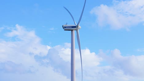 Side-view-of-large-windmill-turbine-blades-spinning-against-blue-sky-with-white-clouds