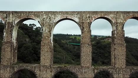 Drone-flight-shot-crossing-one-of-the-arches-of-the-historic-site-"Arcos-del-Sitio"-in-Tepotzotlán,-State-of-Mexico,-Mexico