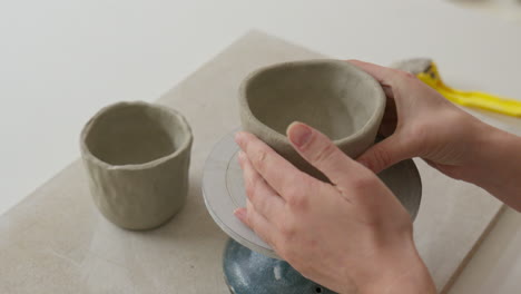 Placing-clay-cup-on-a-turning-wheel,-preparing-for-crafting-in-a-charming-studio