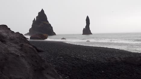Majestic-moody-view-of-spiked-rocks-in-the-ocean-with-an-overcast-sky-at-Reynisfjara-Black-Sand-Beach-in-Iceland