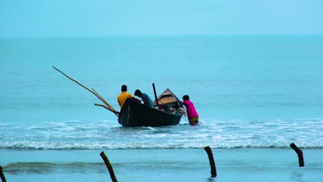 A-fisherman-pulling-a-local-fishing-boat-with-fishermen-in-it,-to-put-it-in-the-seawater