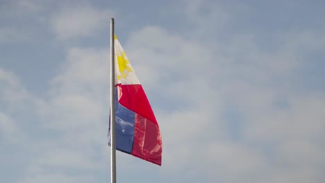 Bandera-Filipina-Ondeando-Al-Viento-En-Un-Asta-De-Bandera-Contra-Un-Cielo-Azul-Ligeramente-Nublado