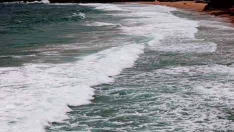 Coastal-waves-rhythmically-approaching-a-sandy-beach,-A-dance-of-sea-and-shore-under-a-cloudy-sky