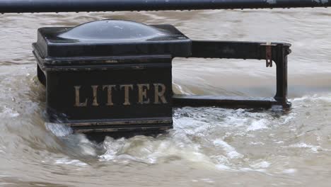 Close-up-of-flood-water-from-the-River-Severn-flowing-around-a-litter-bin-at-Bewdley