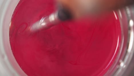 Top-down-view-of-red-paint-releasing-and-spreading-across-water-from-brush-swirling