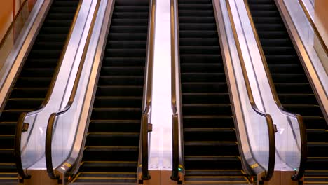 An-escalator-with-black-steps,-ascending-into-a-bright-light,-flanked-by-reflective-metallic-handrails-in-a-quiet,-empty-setting