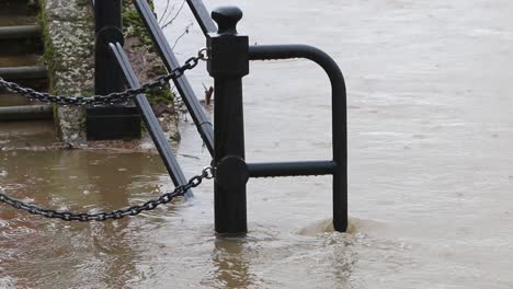 Der-Fluss-überschwemmt-Das-Geländer-Und-Den-Fußweg-An-Seinen-Ufern,-Während-Mehr-Regen-Fällt