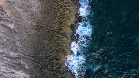 Aerial-satellite-view-pans-across-rocky-jagged-volcanic-shoreline,-nature-background