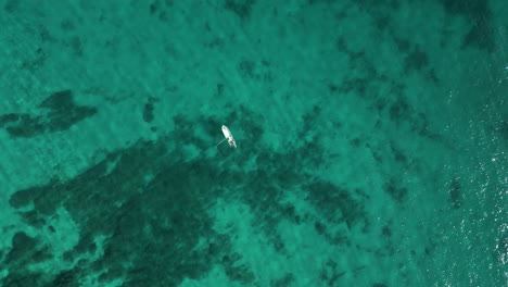 Lone-boat-floating-on-wide-open-turquoise-ocean---Drone-top-down-view