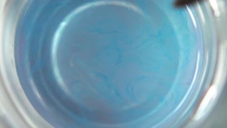 Blue-paint-disperses-from-hairs-of-watercolor-paintbrush-as-it-is-swirled-in-clean-water-cup