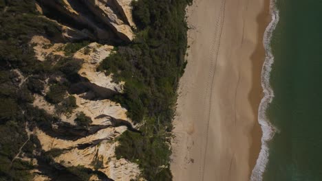 Drone-shot-of-cliff,-sand-and-sea-on-Fonte-da-Telha-beach-with-footprints-in-the-sand