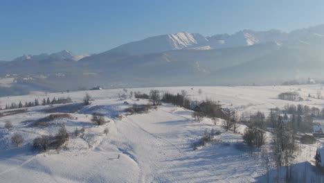 Winter-landscape-of-Tatra-mountain-peaks,-village-and-snow-covered-pastures,-aerial-view