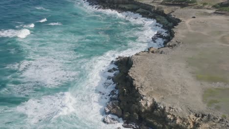 High-angle-bird's-eye-view-of-strong-ocean-waves-crashing-turquoise-blue-water-on-rocky-shoreline