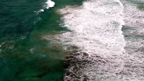 Aerial-shot-of-a-wave's-frothy-crest-breaking-along-the-shoreline,-The-sea's-lace-like-foam-meeting-the-beach