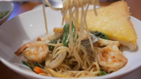 Twisting-some-seafood-spaghetti-using-a-fork,-which-is-served-on-a-platter-filled-with-pasta,-seafood,-and-some-spices