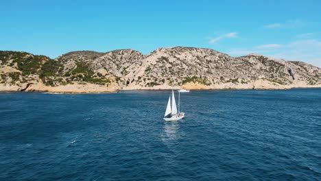 Sailboat-sails-across-open-ocean-water-as-drone-pullsback-revealing-stunning-landscape