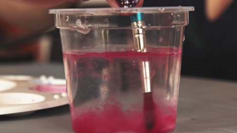 Der-Aquarellpinsel-Gibt-Beim-Eintauchen-In-Einen-Wasserbecher-Einen-Spritzer-Roter-Farbe-Ab