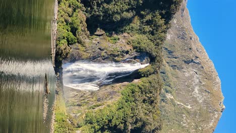 Cruising-by-majestic-Lady-Bowen-waterfall,-Milford-Sound,-New-Zealand,-vertical-shot