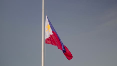 Large-Philippine-flag-on-giant-flagpole,-with-birds-flying-past-in-slow-motion